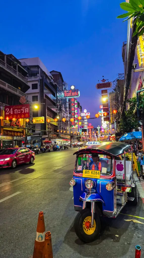 Busy Bangkok street at night with tuk tuk, neon lights, and city traffic.