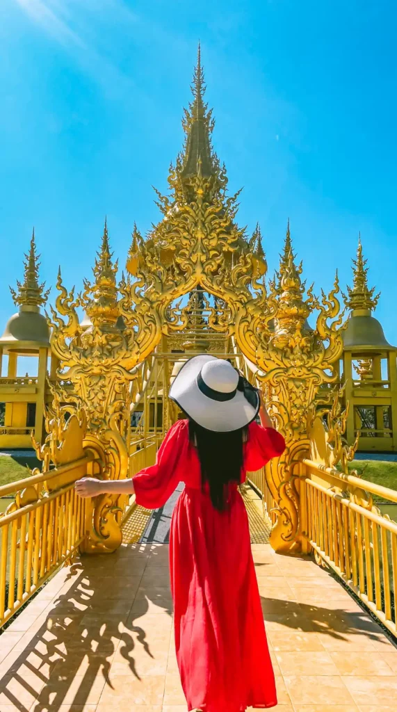 Visitor walking toward an ornate Thai temple surrounded by golden architecture in northern Thailand.