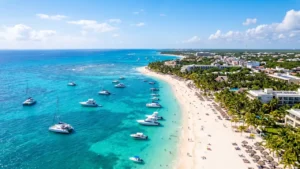 Aerial view of Playa del Carmen's turquoise Caribbean coastline with white sandy beaches, boats, palm trees, and sunshine.