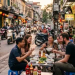 Foreigners and locals enjoying street food on small plastic stools in Hanoi, Vietnam, showcasing everyday life in the city.